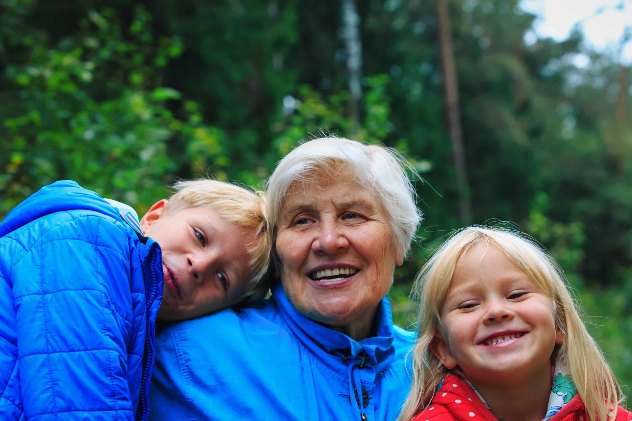 A smiling elderly woman with two young children outdoors, embodying the spirit of grandparent sponsorship in Canada.