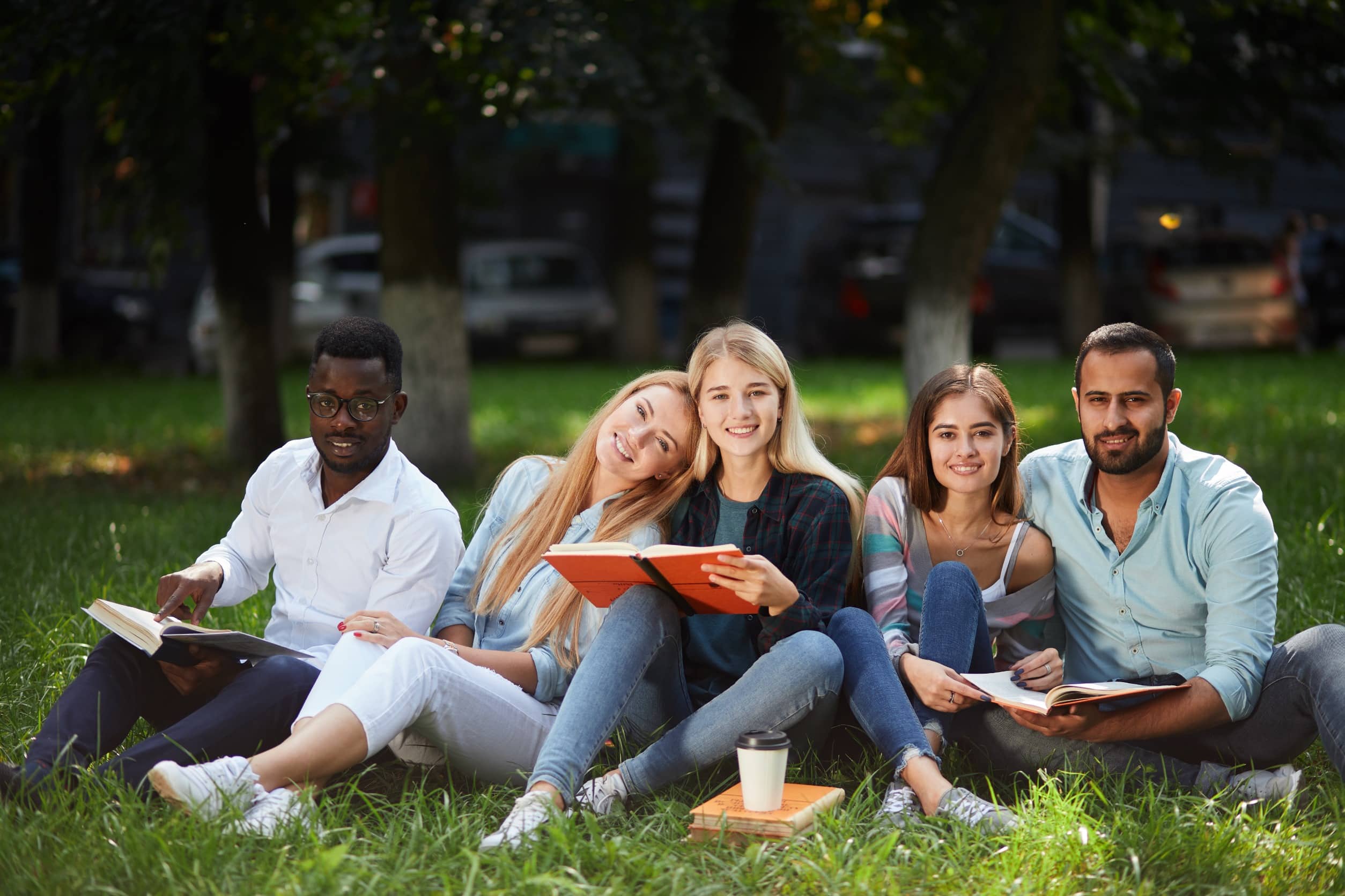 A diverse group of students studying and relaxing in a park, some holding their Canada student visa documents.