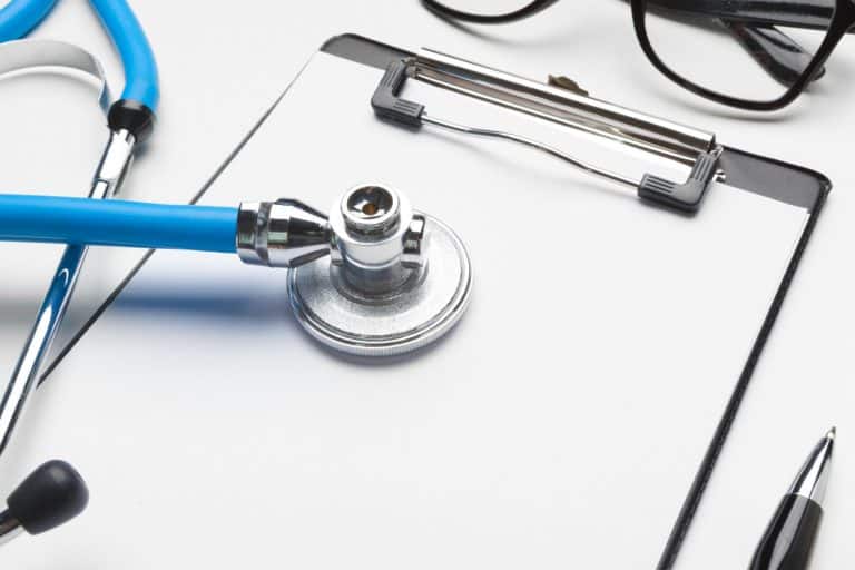 A stethoscope, clipboard, glasses, and pen arranged on a white surface, suggesting a medical professional's workspace in the context of Canada's medical immigration.