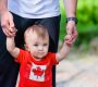 A toddler in a Canadian flag t-shirt holding hands with a family sponsor.