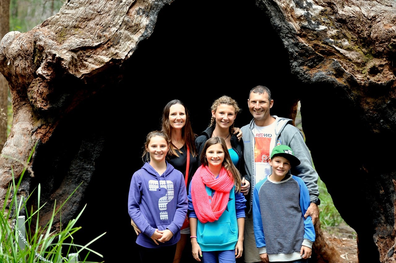 A Canada Family Class applicants posing together in front of a large hollow tree trunk.
