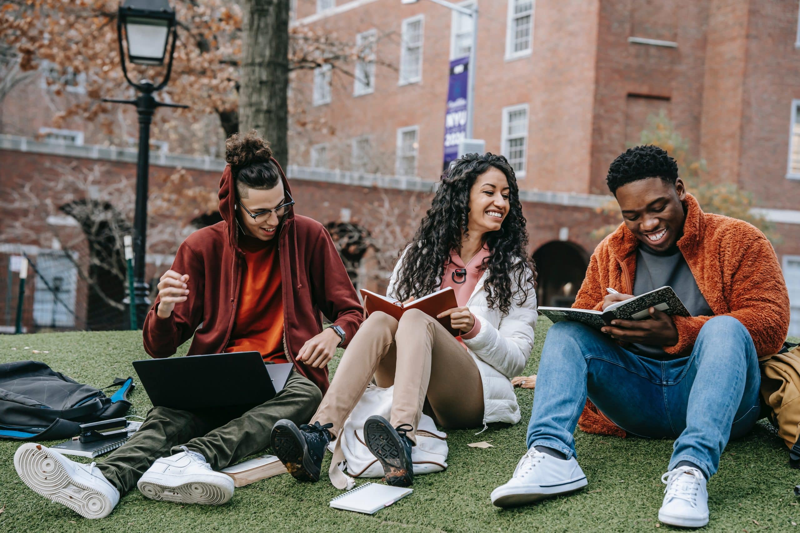 Three students studying and sharing ideas outdoors on a campus lawn in Canada.
